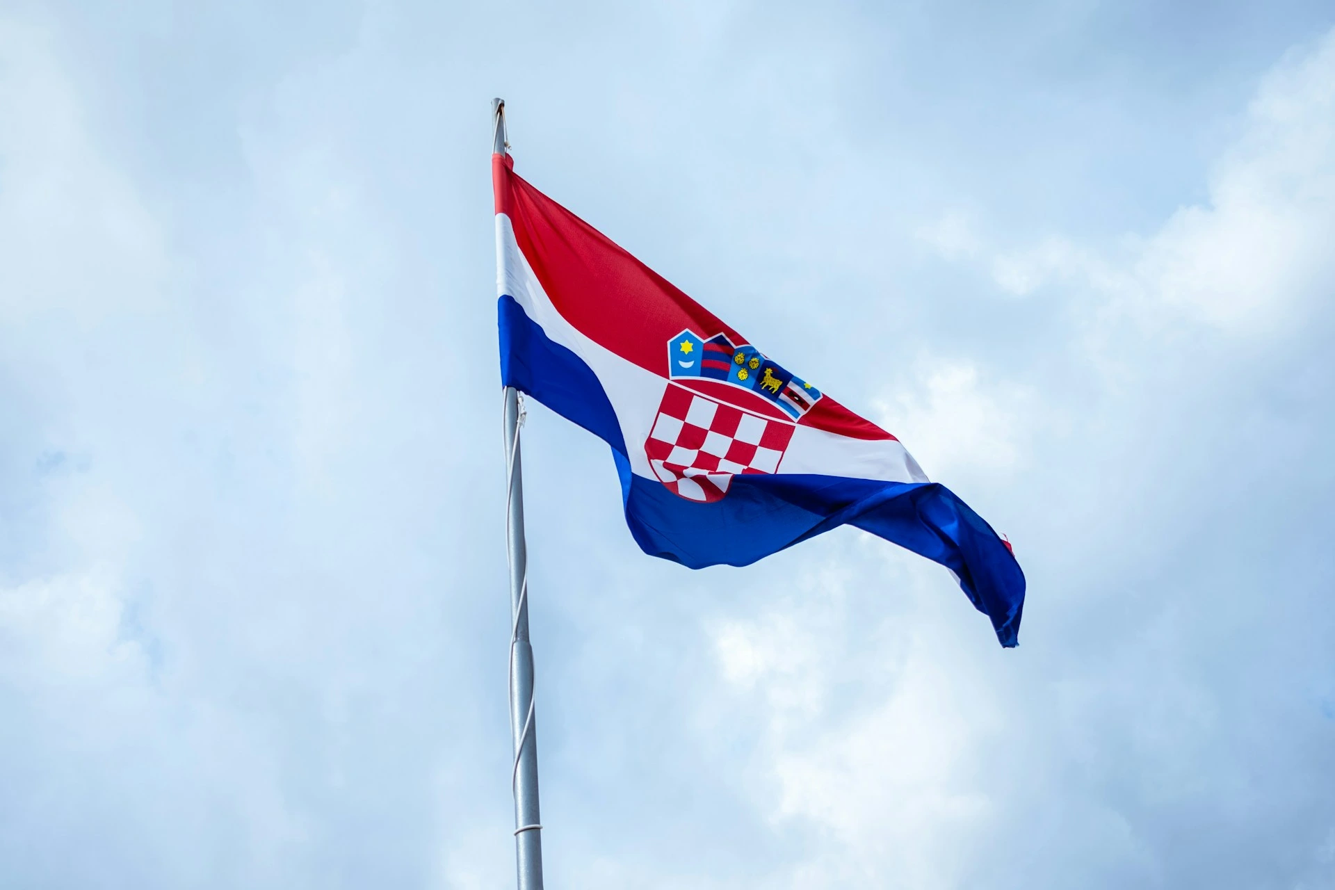The national flag of Croatia waving against a cloudy blue sky.